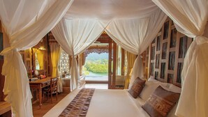 Un dormitorio amplio con una cama grande, un escritorio de madera y vistas a un jardín exuberante a través de un vano abierto.
