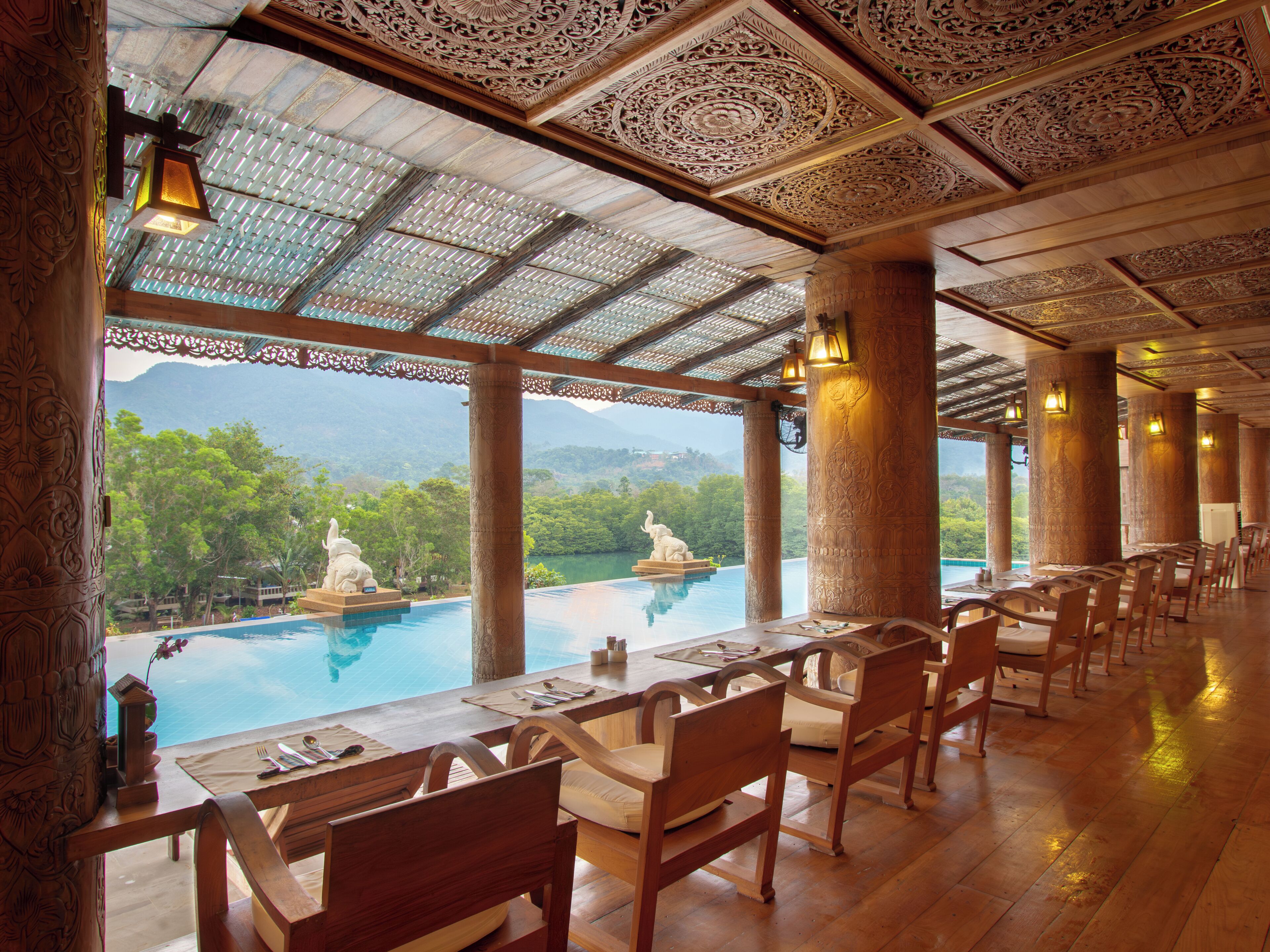 A restaurant with a pool view, wooden furniture, and ornate ceiling details.