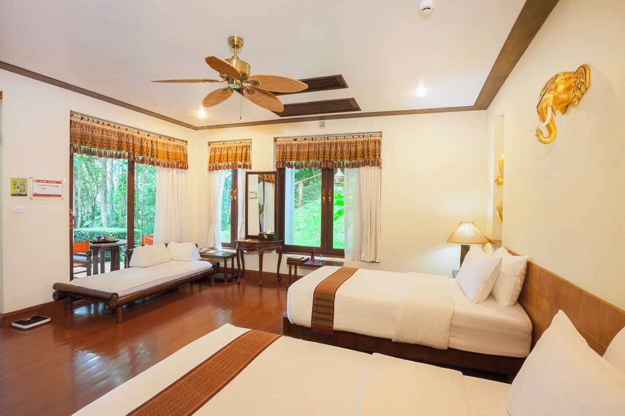 A hotel room with a bed, a desk, and a chair. There are curtains on the windows, and a ceiling fan is visible.