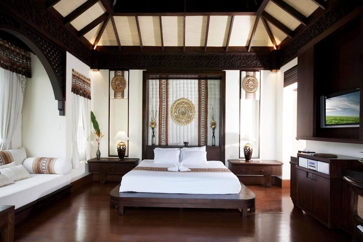 Um quarto espaçoso com uma cama grande, piso de madeira e um teto alto com claraboias.