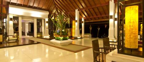 A spacious lobby with a high ceiling, a central planter with greenery, and a seating area with chairs.