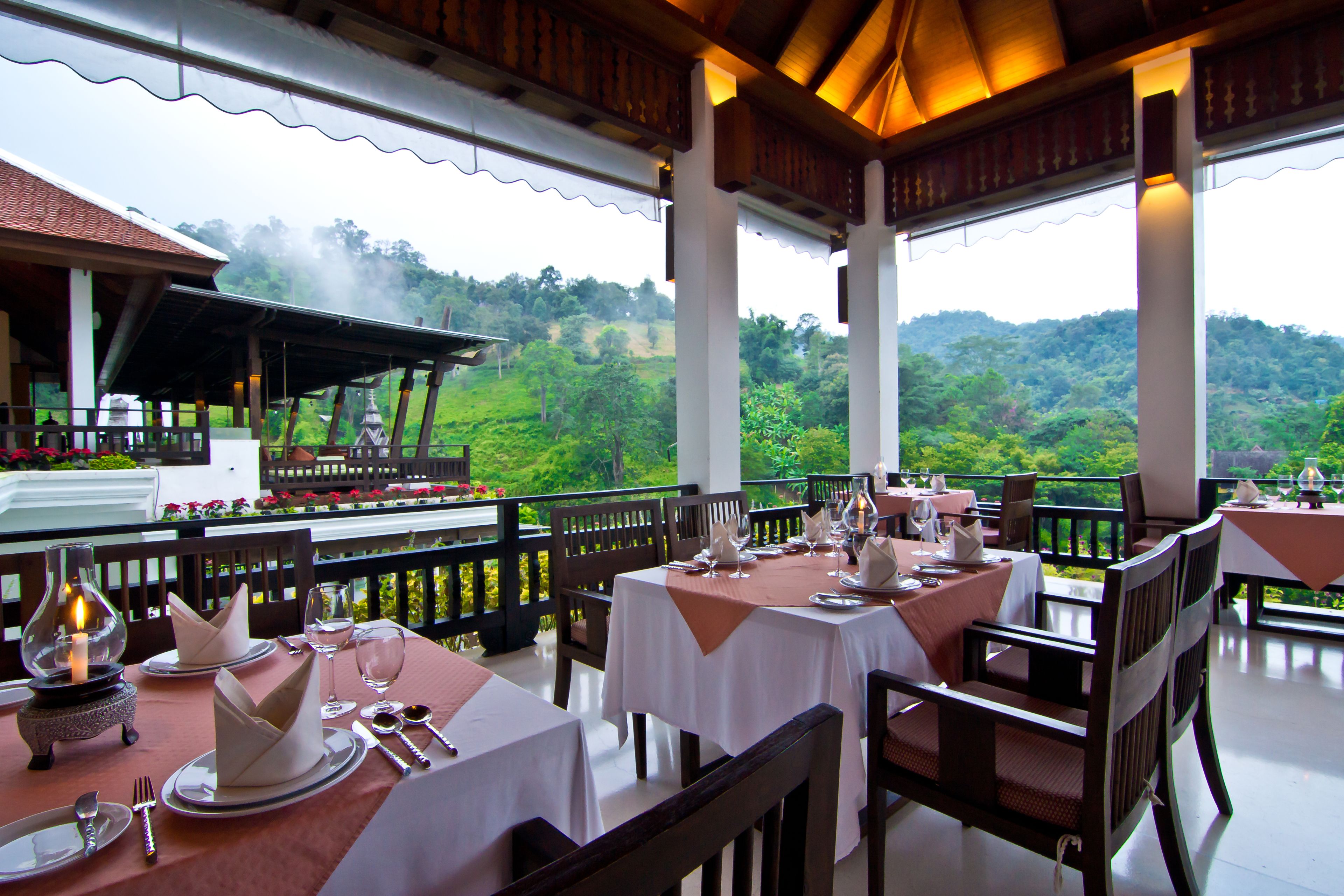 A restaurant with tables set for dining, overlooking a lush green landscape.