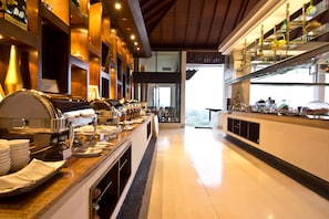 A buffet setup with multiple serving stations, a polished marble countertop, and a view of the outdoors through a large window.