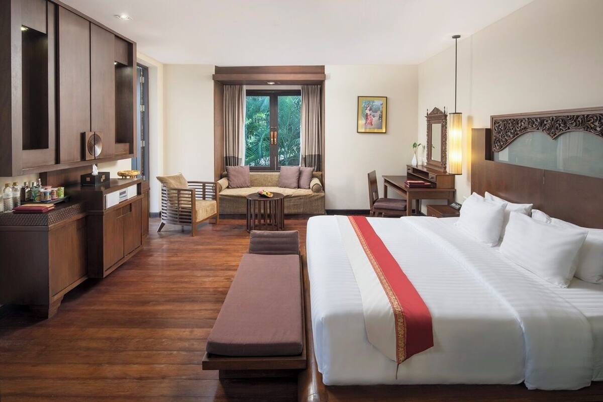 Quarto de hotel com uma cama grande, sofá, escrivaninha e área de refeições.