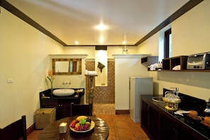 A compact kitchen with a sink, stove, and microwave. There is a dining table with a fruit bowl and a candle.