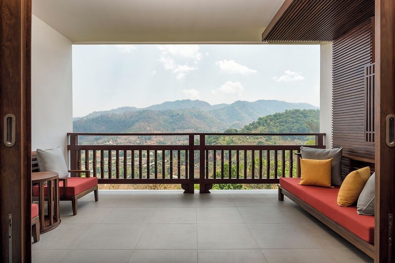 Un balcon avec une balustrade en bois, un canapé rouge avec des coussins et une petite table.