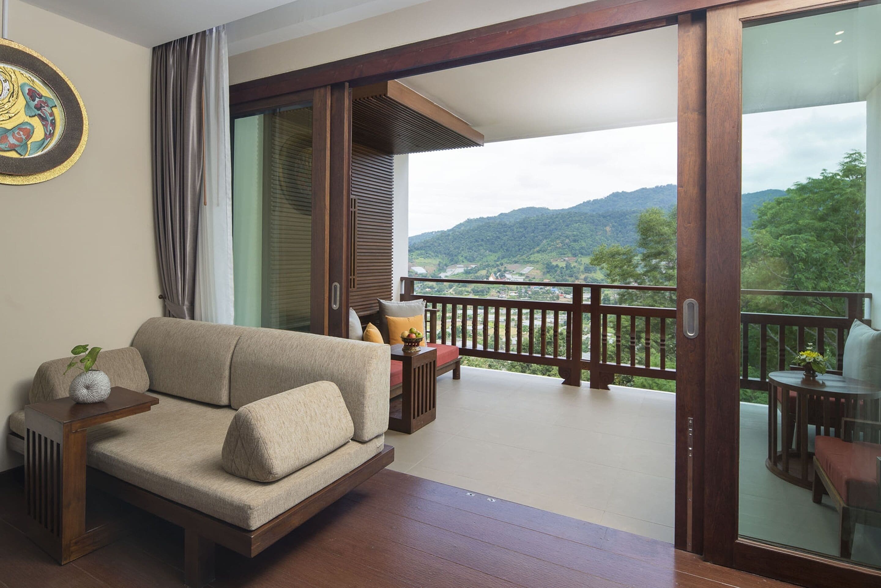 A balcony with a sofa, a small table, and a chair. The balcony overlooks a mountainous landscape.