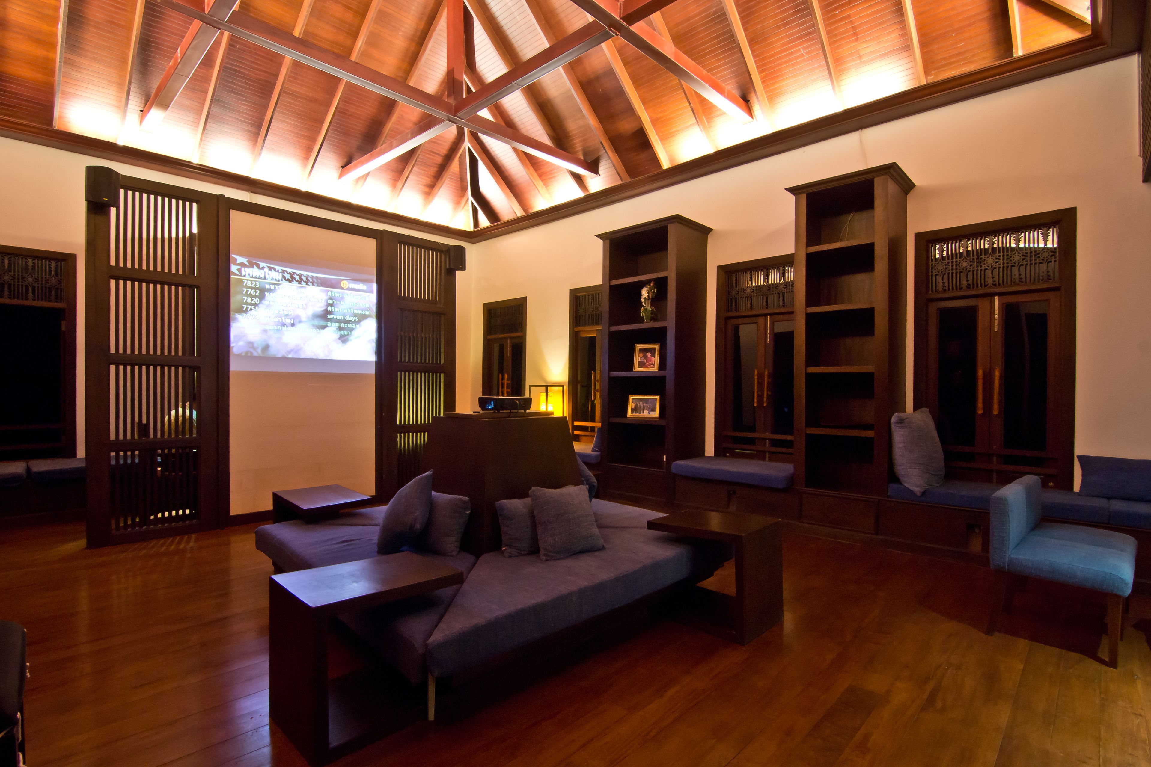 A spacious living area with a wooden ceiling, built-in bookshelves, a sofa, and a TV screen displaying a map.
