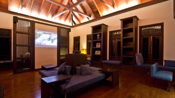 A spacious living area with a wooden ceiling, built-in bookshelves, a sofa, and a TV screen displaying a map.