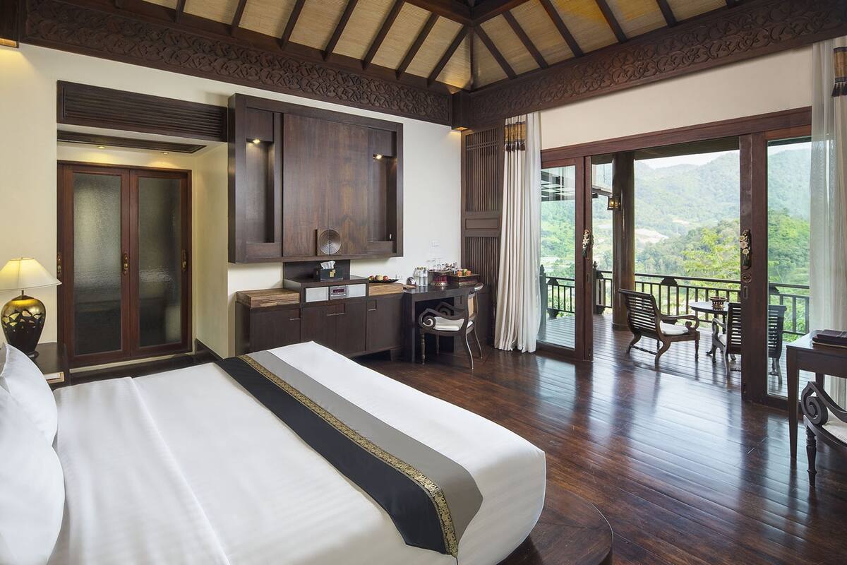 Quarto de hotel com uma cama grande, uma escrivaninha e uma varanda com vista para as montanhas.