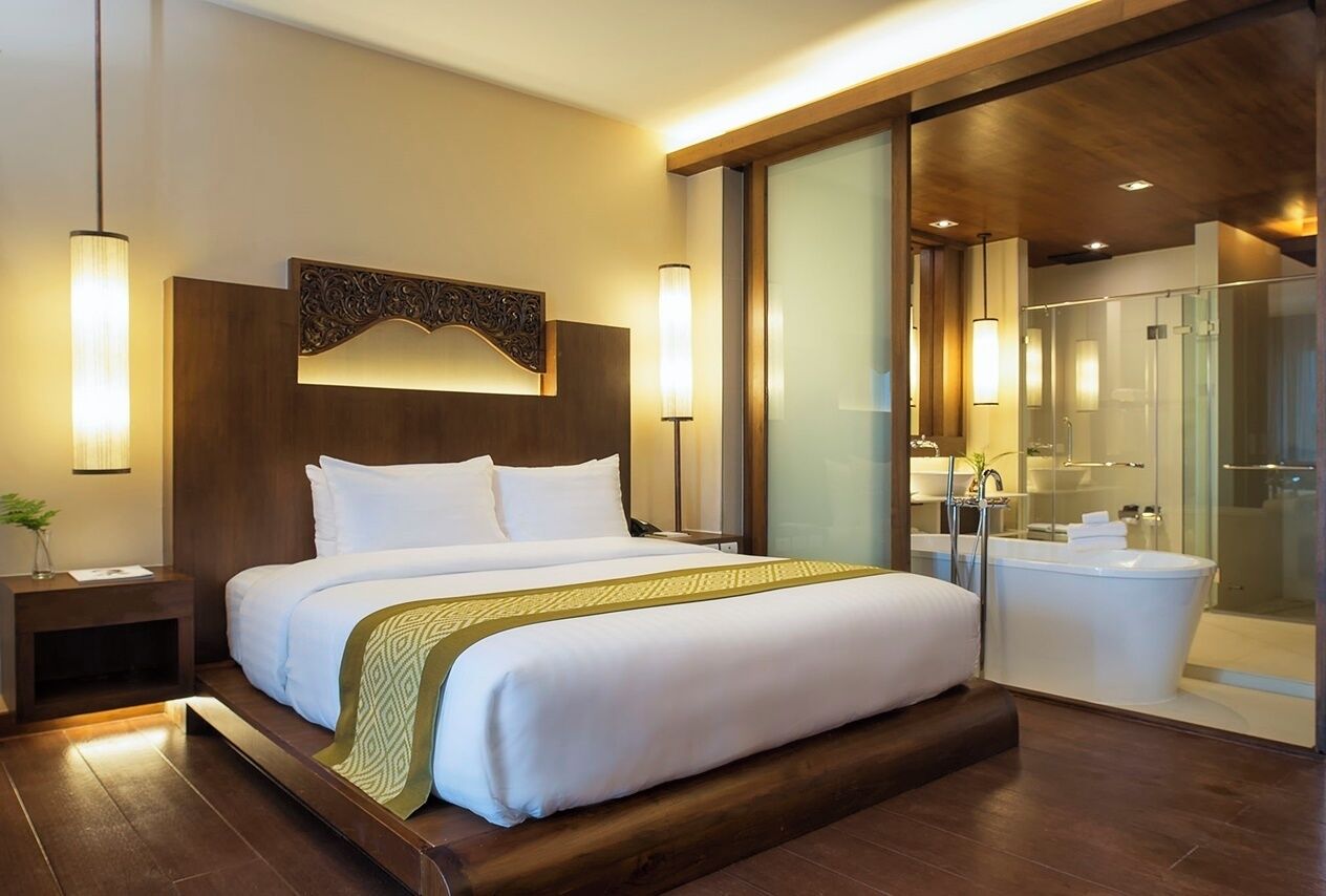 Habitación de hotel moderna con una cama grande, ducha con cerramiento de vidrio y cabecero de madera.