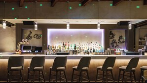 A bar area with a long counter, multiple stools, and a variety of bottles and glasses. - Axos Hotel (Rethymno)