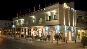 A hotel with a prominent sign, outdoor seating, and multiple flags. - Axos Hotel (Rethymno)