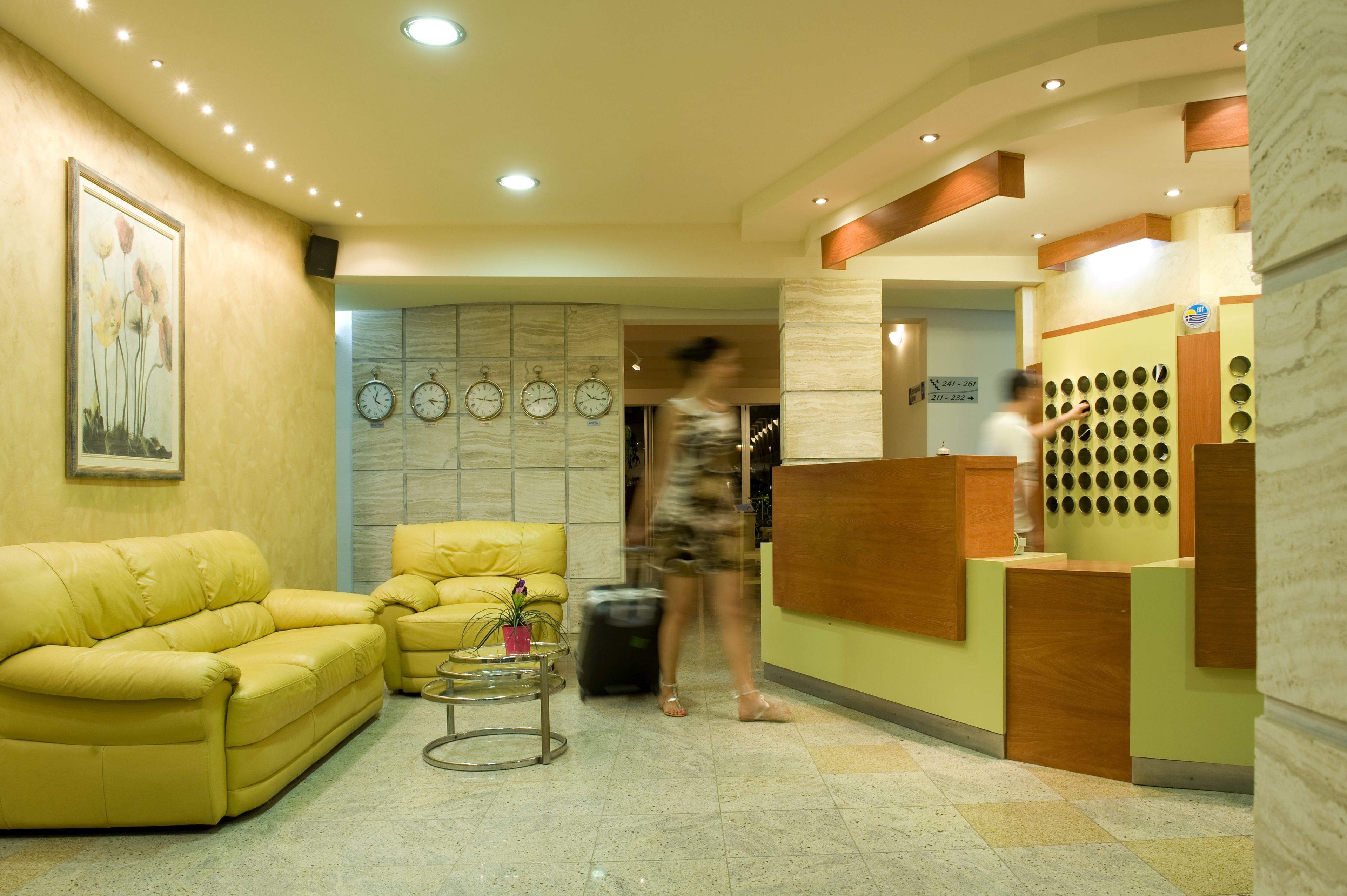 A hotel reception area with a yellow sofa, a small table with a plant, and a reception desk with a circular design.