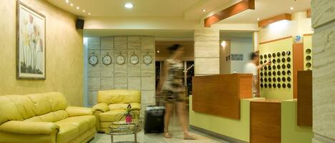 A hotel reception area with a yellow sofa, a small table with a plant, and a reception desk with a circular design.