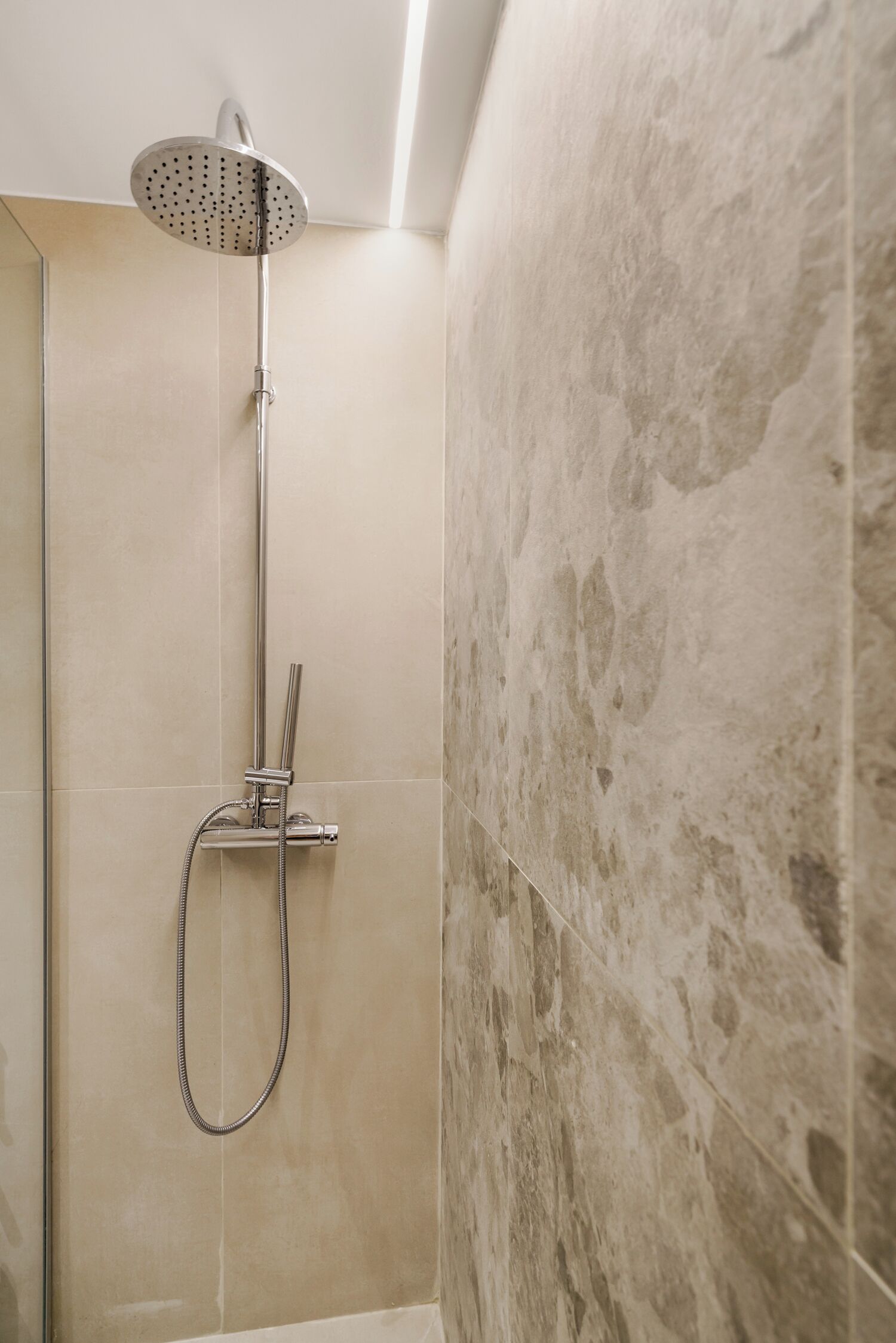 A shower with a handheld showerhead and a fixed overhead showerhead, mounted on a wall with a textured tile design.