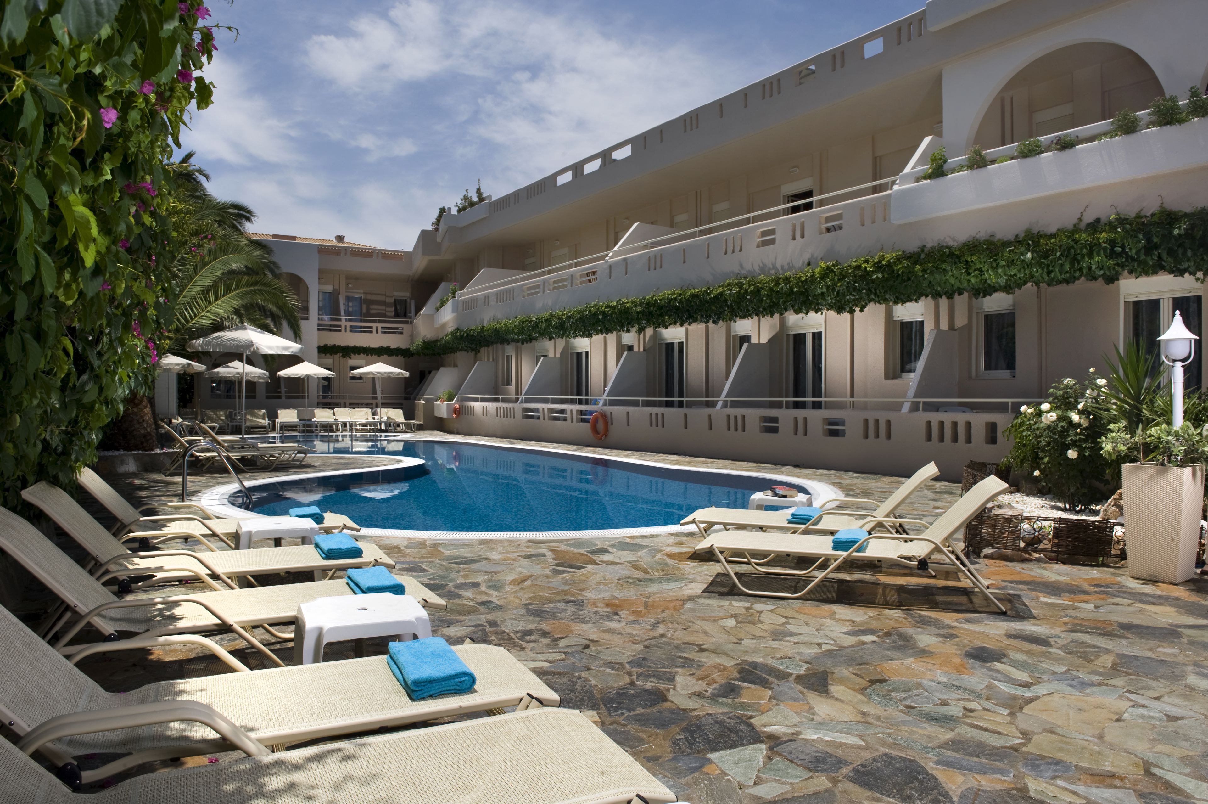 A pool area with lounge chairs and umbrellas, surrounded by stone flooring and greenery.