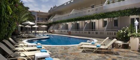 A pool area with lounge chairs and umbrellas, surrounded by stone flooring and greenery.