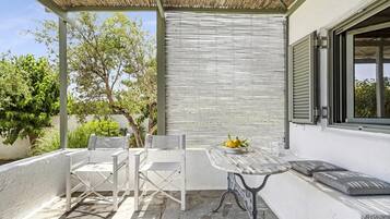 Un patio al aire libre con mesa y sillas, una pérgola y vistas a árboles y un edificio.