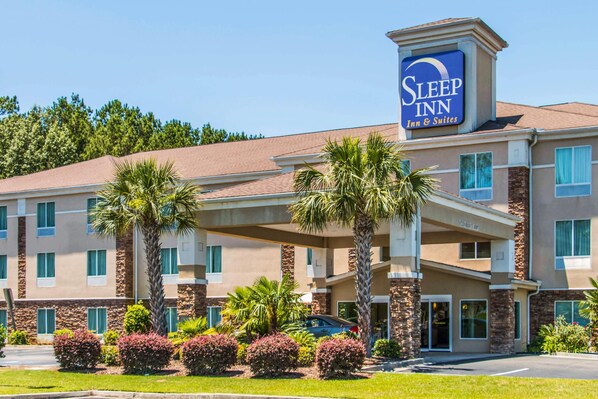 A Sleep Inn hotel with a covered entrance, palm trees, and a clear blue sky.