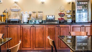 Un bar pour prendre le petit-déjeuner, équipé d’une machine à café, d’un grille-pain et d’un panier de fruits. On aperçoit en arrière-plan des meubles en bois et un réfrigérateur.