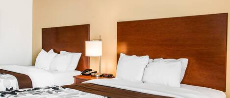 A hotel room with two beds, a nightstand with a lamp, and a telephone.