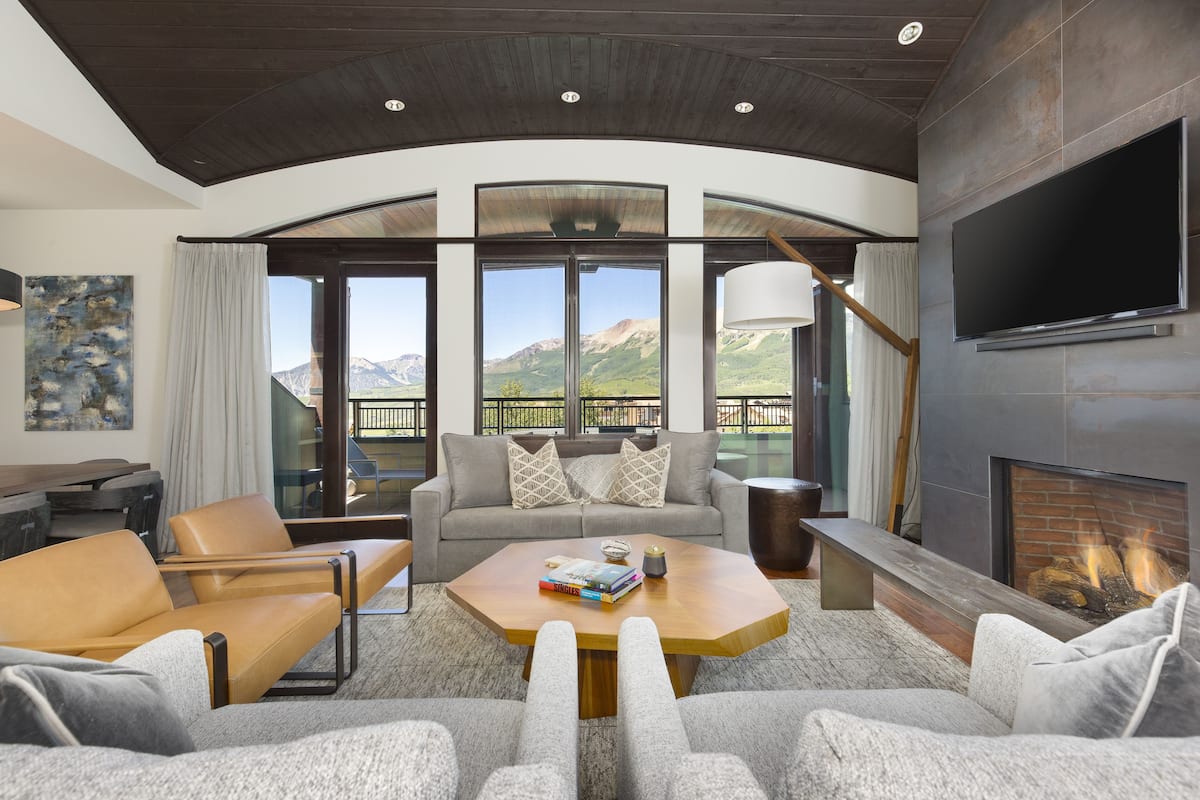 A modern living room with a fireplace, large windows, and a view of mountains.