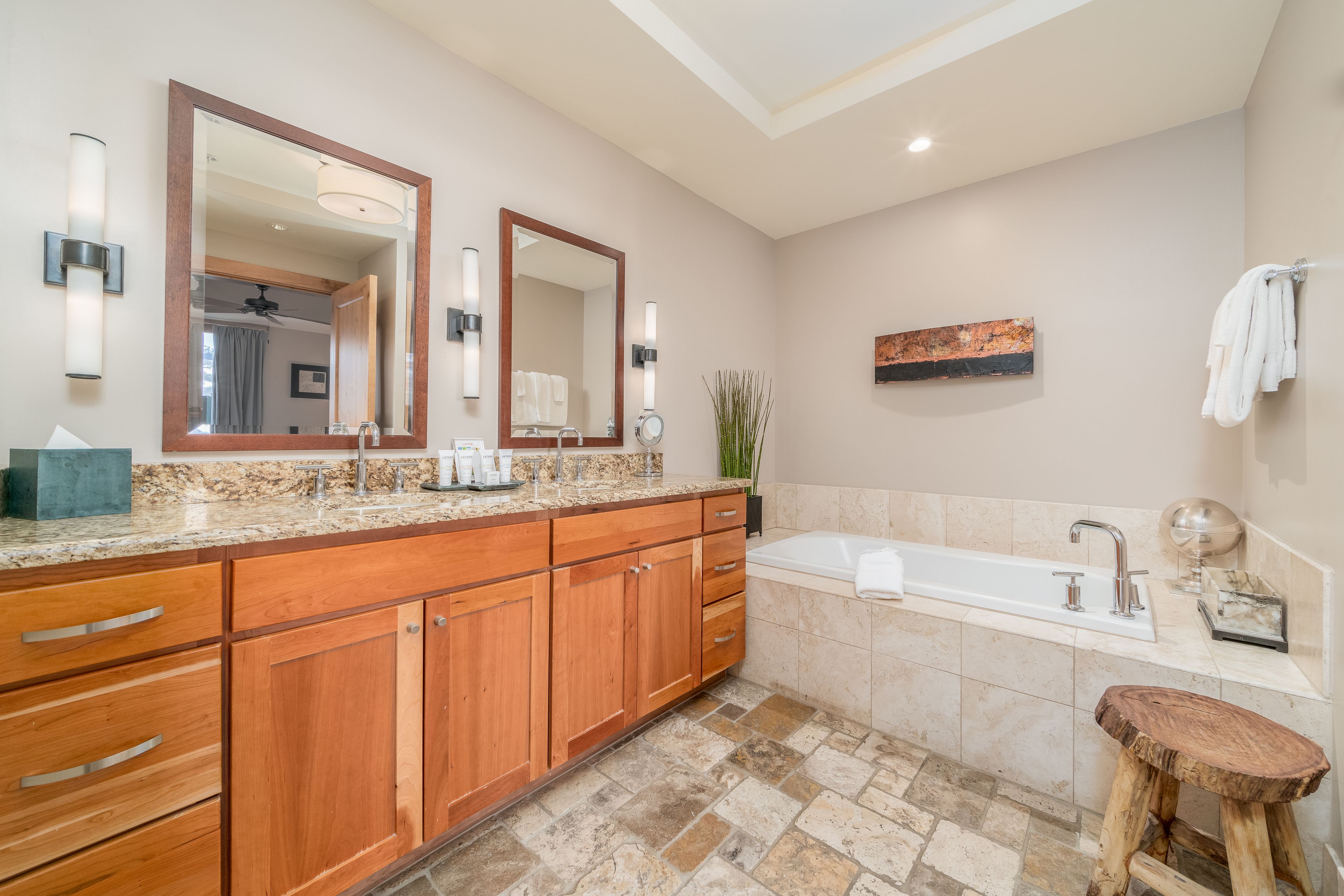 A modern bathroom with a large vanity, a freestanding bathtub, and a wooden stool.