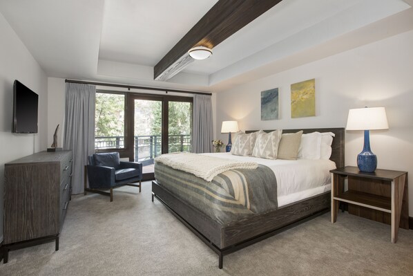 A bedroom with a large bed, a desk, a chair, and a TV on the wall.