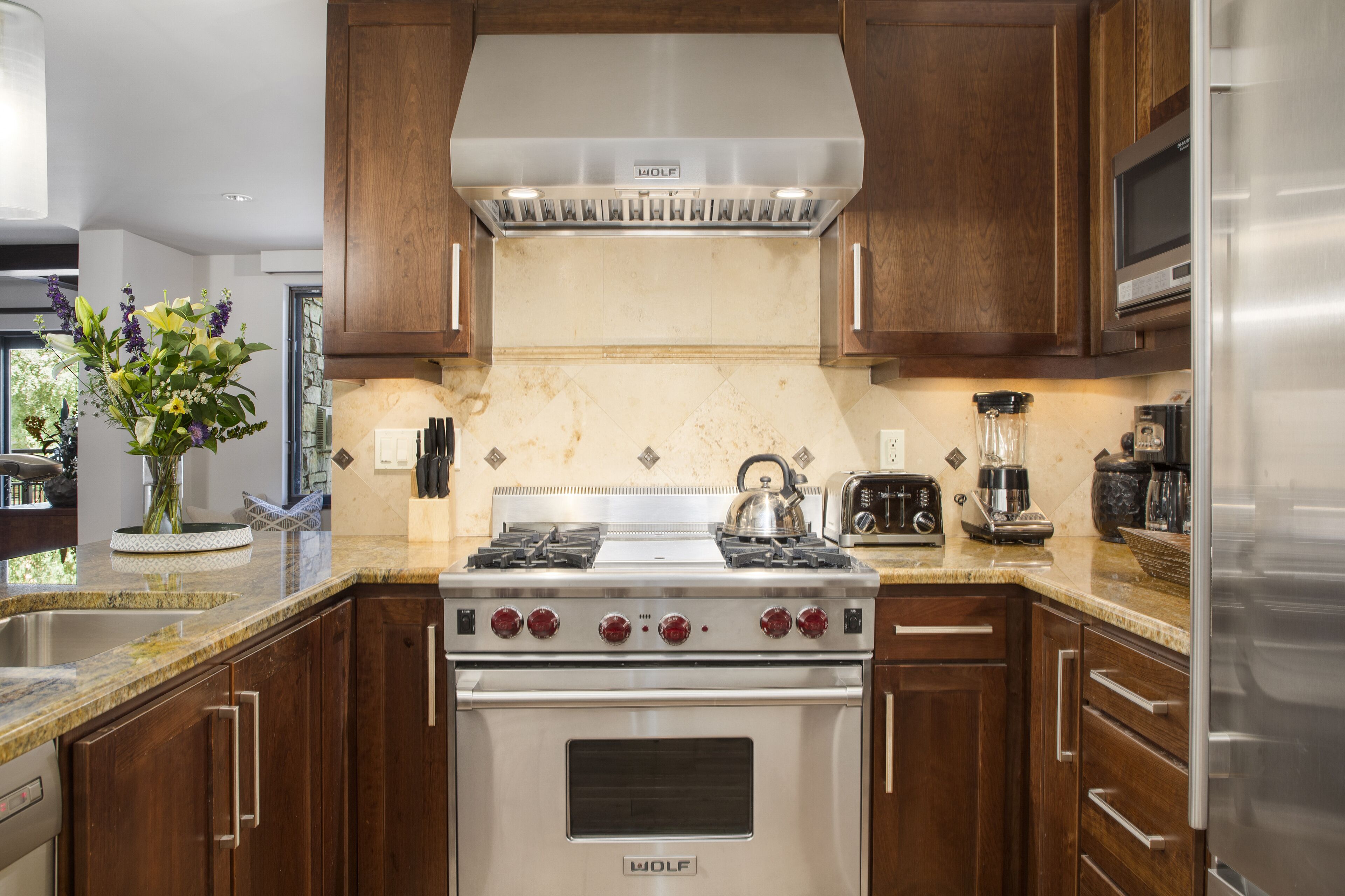A kitchen with a Wolf stove, a stainless steel refrigerator, wooden cabinets, and a granite countertop.