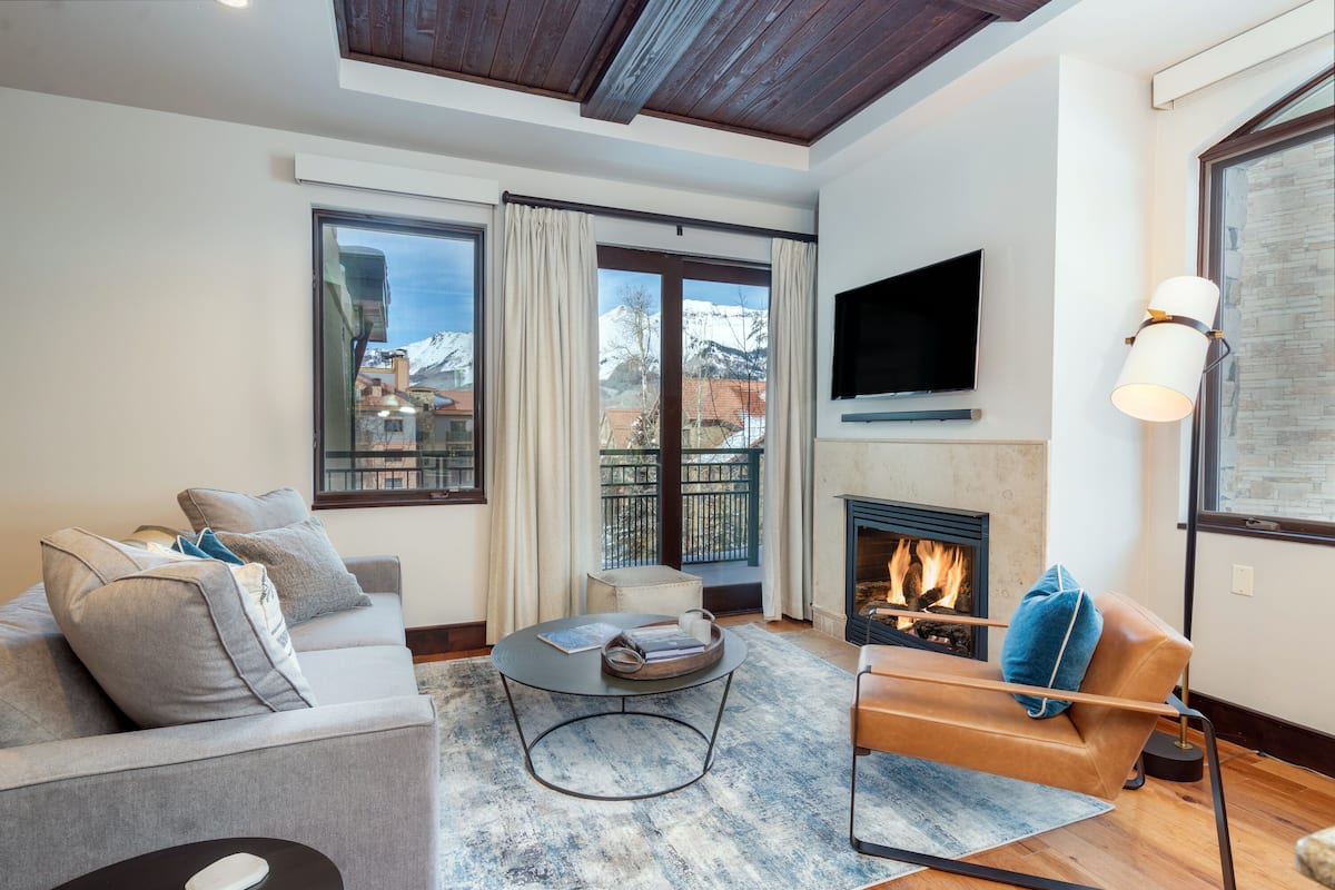 A modern living room with a fireplace, a sofa, a coffee table, and a TV mounted on the wall.
