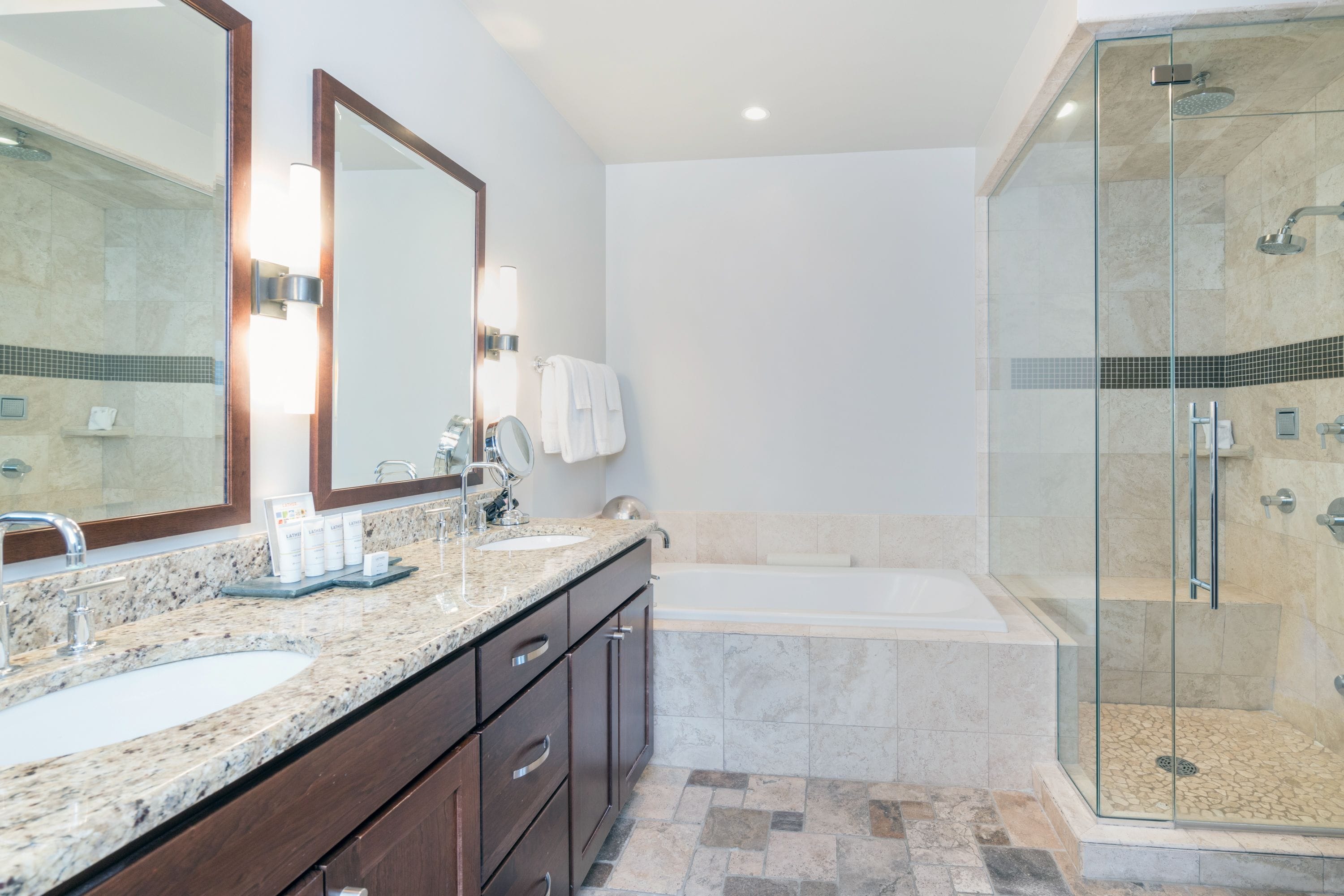 Ein modernes Badezimmer mit einer Granit-Arbeitsplatte, einem großen Spiegel, einer Badewanne und einer Duschkabine.
