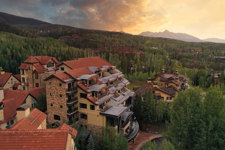 A multi-story hotel with balconies, surrounded by forested mountains.