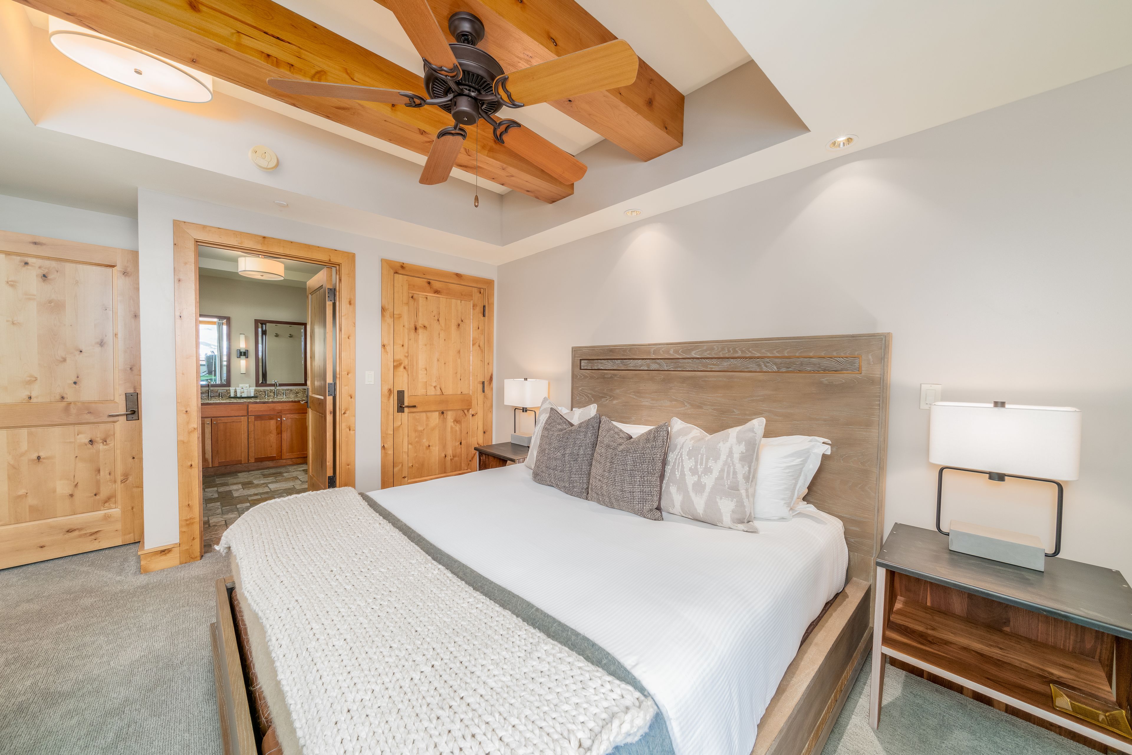 A bedroom with a large bed, wooden headboard, two bedside lamps, and a ceiling fan.
