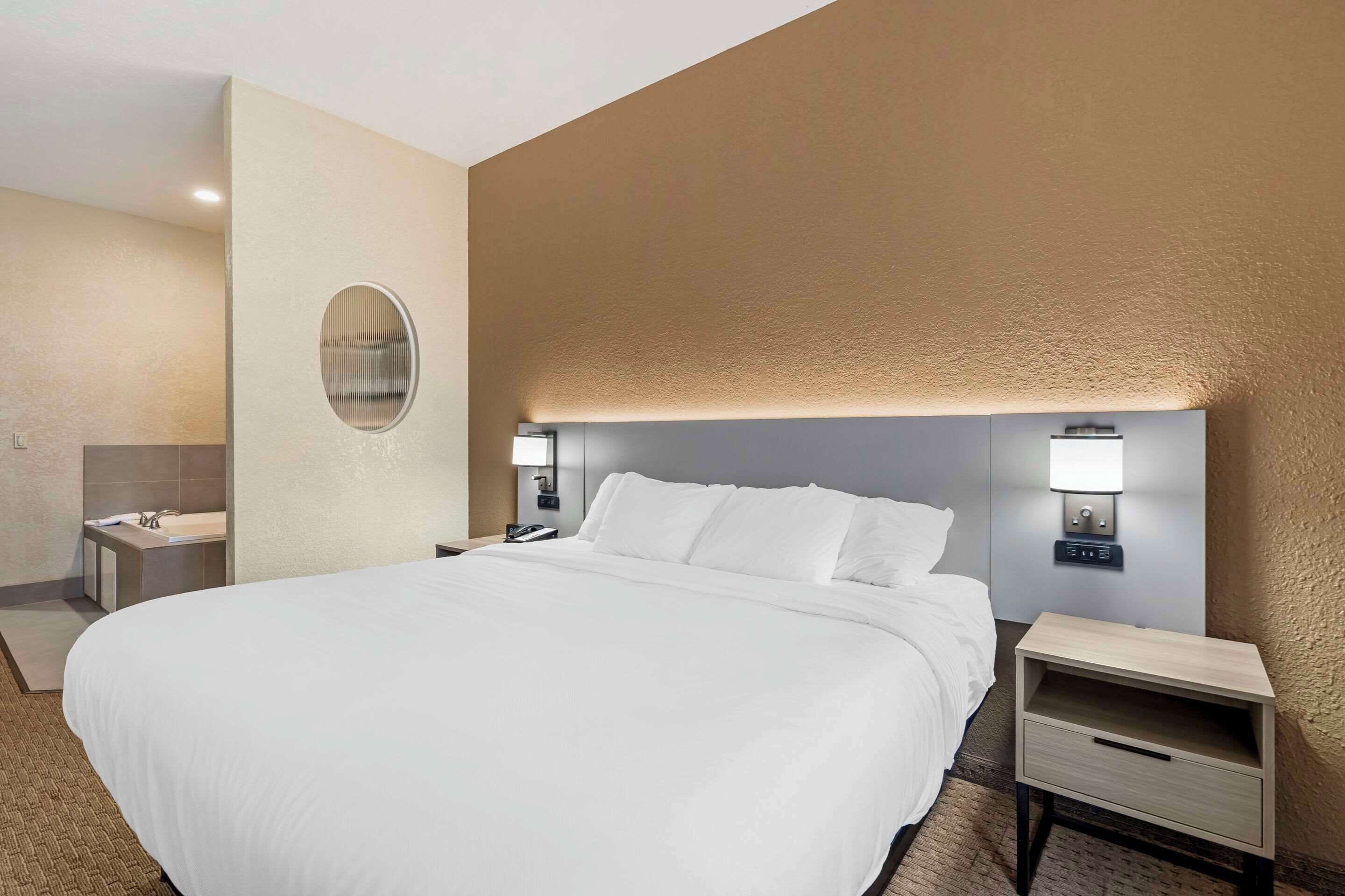 Una habitación de hotel con una cama grande, una mesita de noche, una lámpara de pared y un espejo.