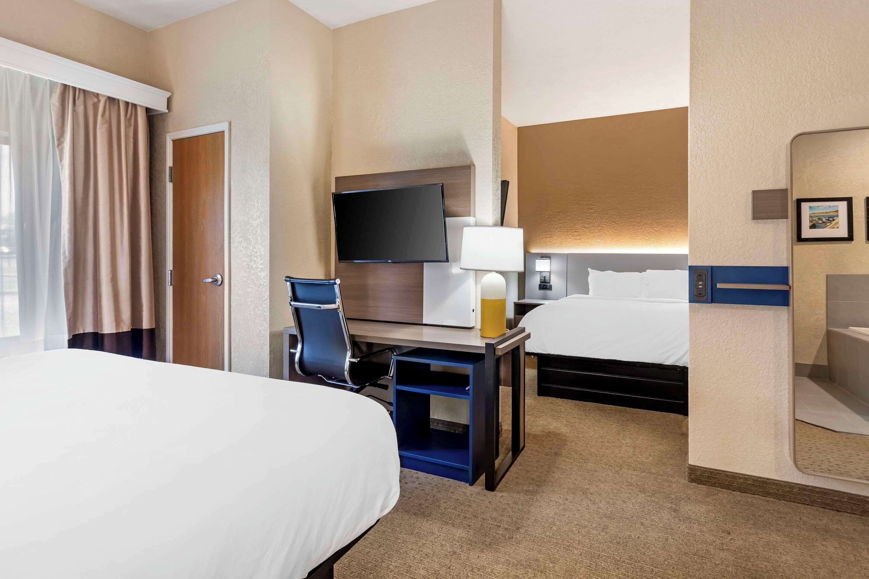 Ein Hotelzimmer mit Bett, Schreibtisch, Stuhl, Fernseher und einem kleinen Tisch mit Lampe.