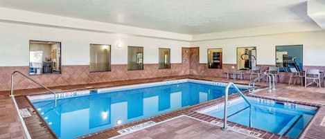 An indoor swimming pool with clear lane markings, a tiled floor, and a seating area with tables and chairs.