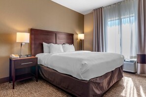 A hotel room with a large bed, two bedside lamps, a nightstand with a phone, and a window with curtains.