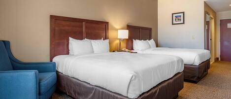 A hotel room with two beds, a desk, a chair, and a ceiling fan.