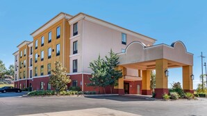 A multi-story hotel with a covered entrance, a parking lot, and a clear blue sky.