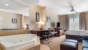 Ein Hotelzimmer mit einer großen Badewanne, einem Schreibtisch mit Stuhl, einem Bett, einem Deckenventilator und einem Fernseher.