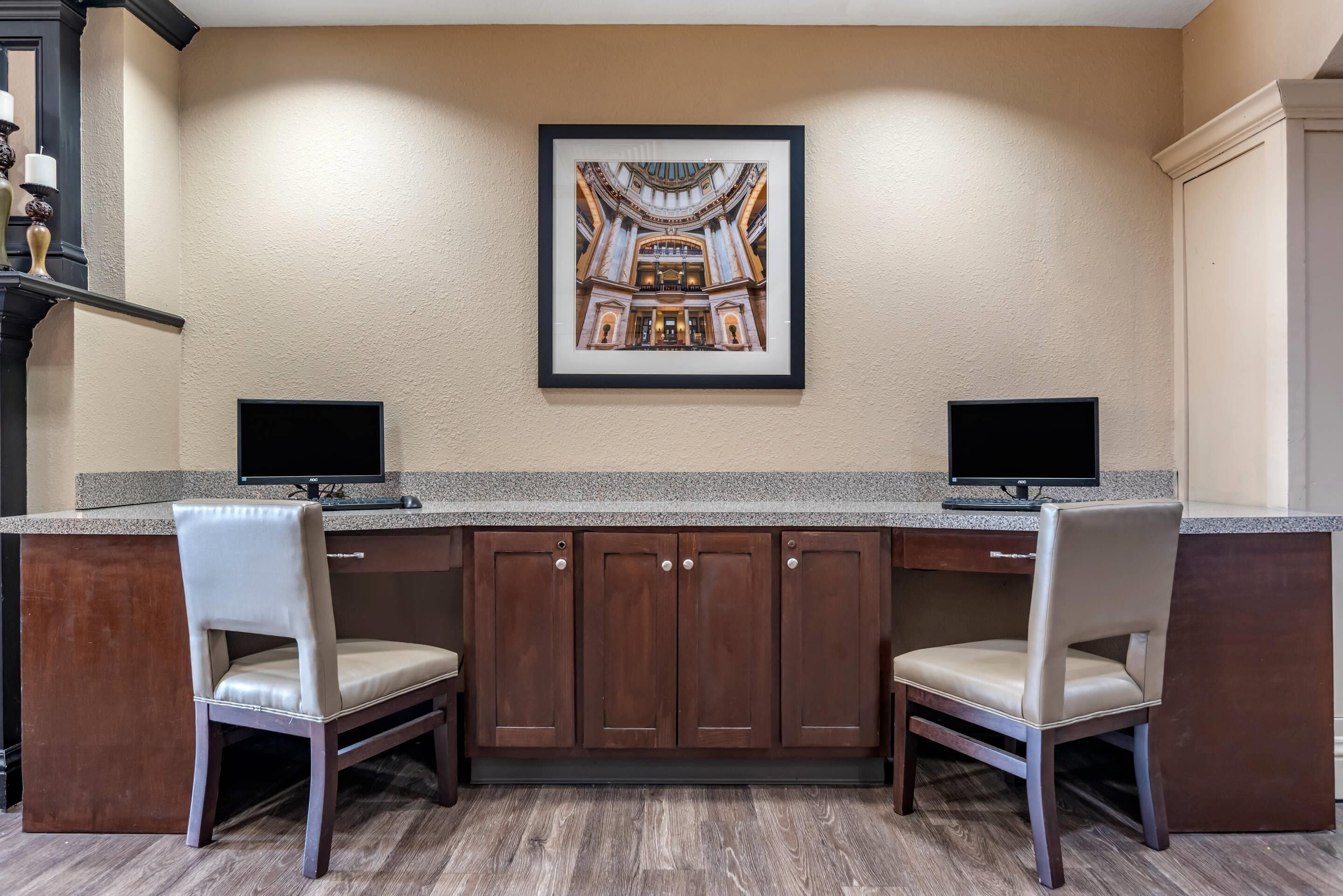 A kitchen with two chairs, a framed picture on the wall, and two monitors on the counter.