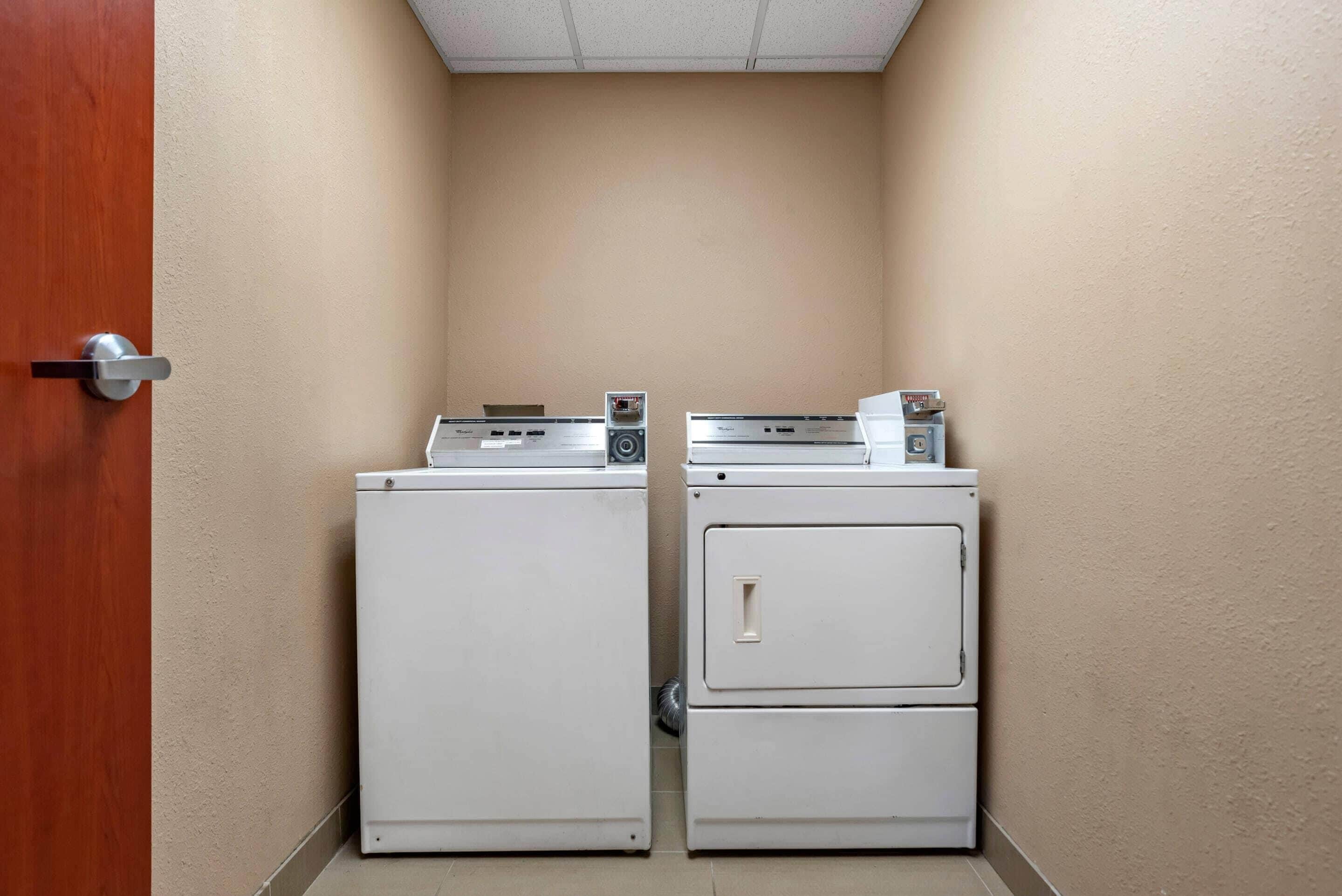 Un cuarto de lavandería con dos lavadoras y secadoras blancos, una puerta de madera y paredes color crema.