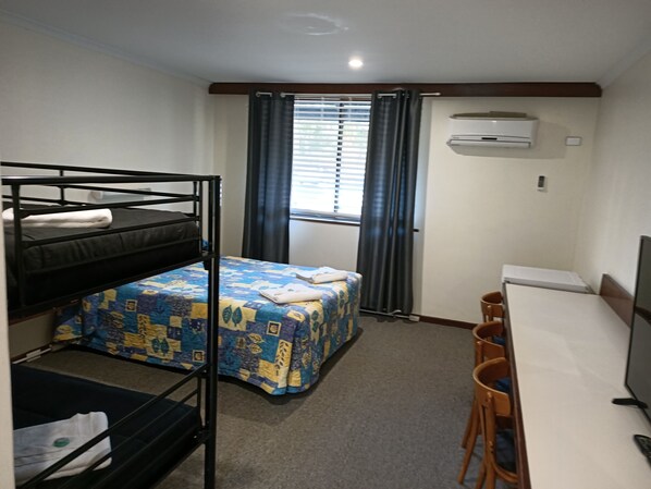 A dormitory room with bunk beds, a desk, and a chair.