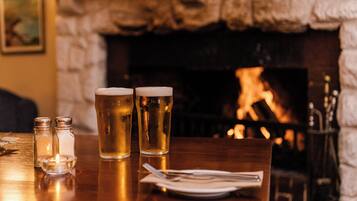 A table with two glasses of beer, salt and pepper shakers, and a plate with cutlery. A fireplace is visible in the background.