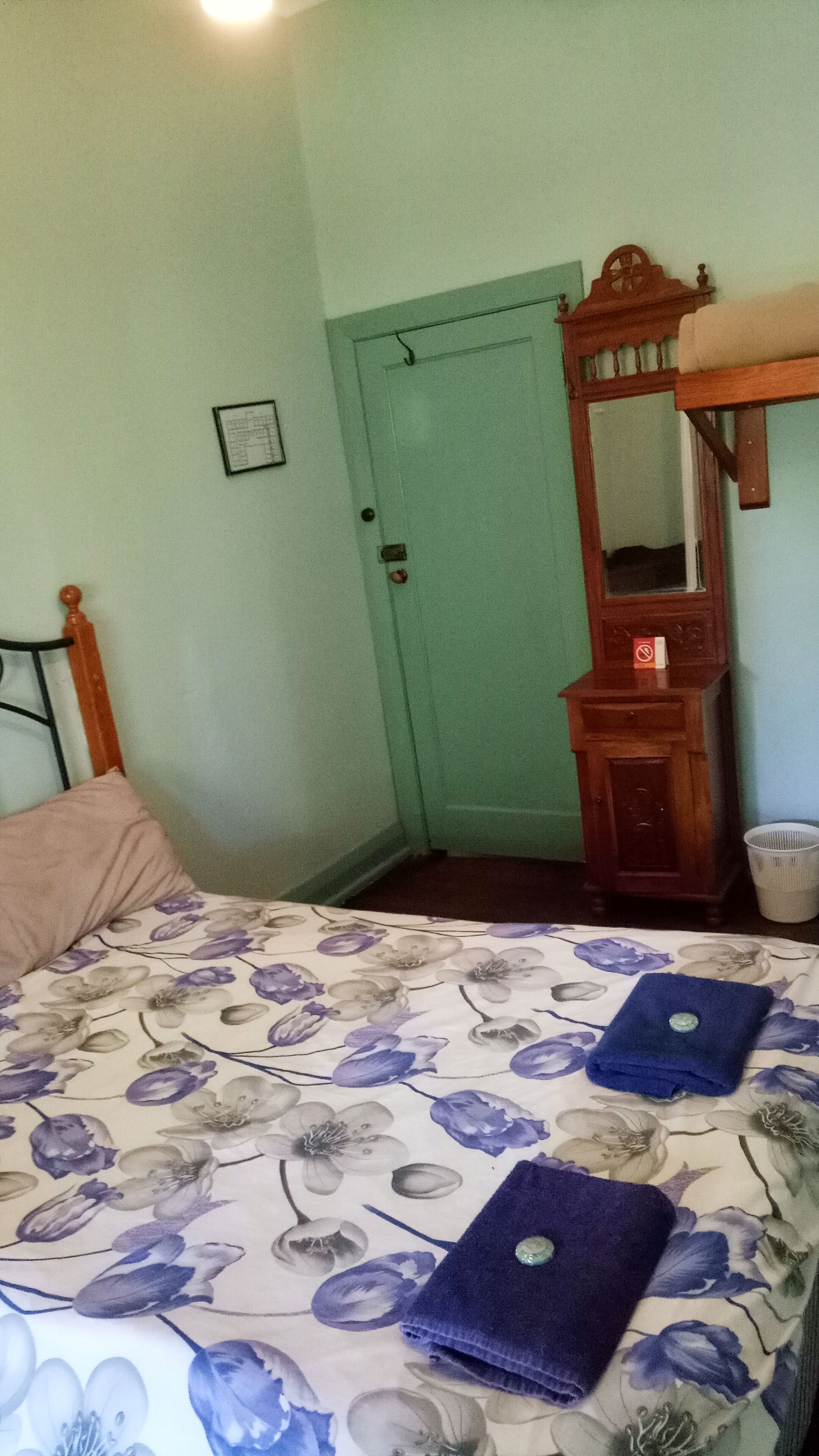 A bedroom with a bed, a wooden dresser, a mirror, and a door.