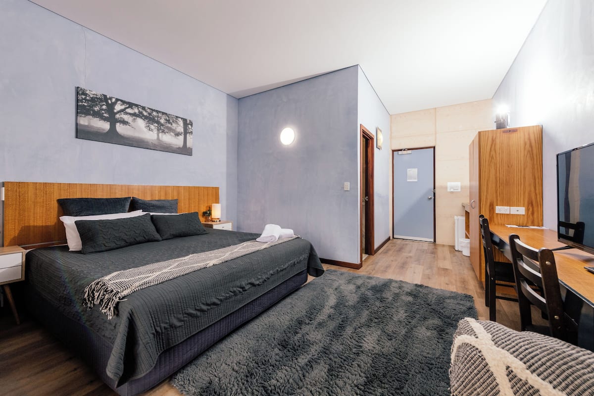 Una habitación de hotel moderna con una cama grande, un cabecero de madera, un televisor de pantalla plana, un escritorio y una zona de comedor.