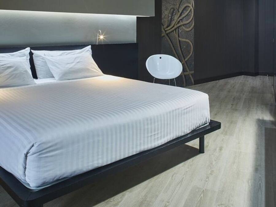 Moderni hotellihuone, jossa on suuri sänky, televisio ja pieni sivupöytä.
