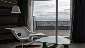A modern room with a white chair, a glass table, and a view of the city through large windows. - Hotel Silken Gran Teatro Burgos (Burgos)