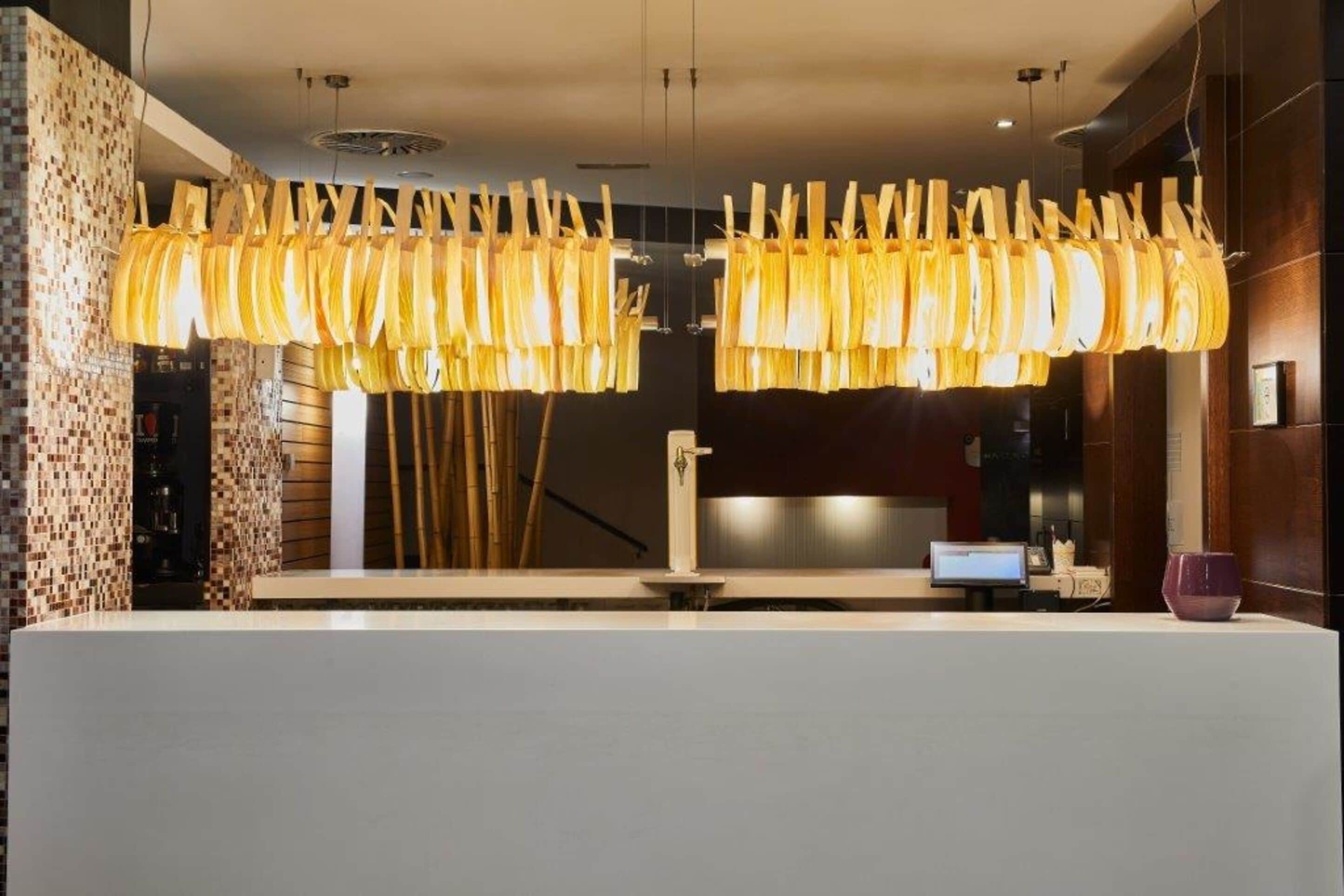 A reception area with a modern design, featuring a large white reception desk, a unique hanging light fixture, and a digital screen.